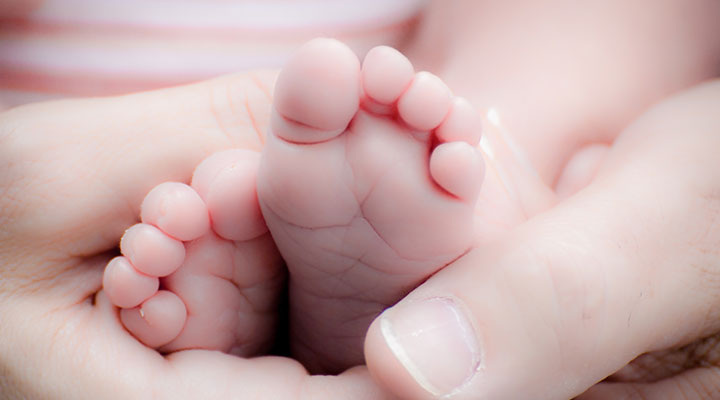 Schuhgröße Baby – Babyfüße in den Händen der liebenden Eltern. Ein guter Moment um die Fußlänge zu messen und die richtige Baby Schuhgröße zu bestimmen