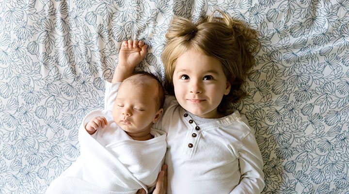 Der kleine Bruder liegt zufrieden im Arm der stolzen großen Schwester. Die richtige Kindergröße bei Kinderkleidung ist wichtig für das Wohlbefinden und den Entwicklungsprozess. Alle Kindergrößen für Kleidung, Mützen, Schuhe und mehr, findest du auf kindergroessen.info