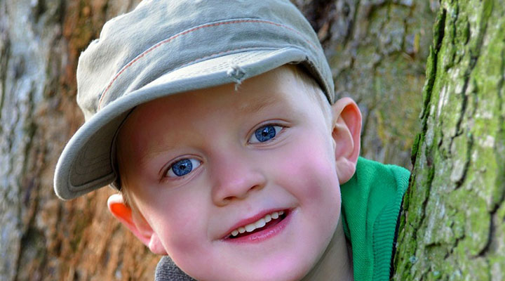 Mützengrößen Kinder – Junge mit Cappi guckt hinter Baum hervor